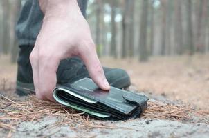 mano masculina recogiendo la billetera perdida de un suelo en el camino de madera de abeto de otoño. el concepto de encontrar algo valioso y buena suerte foto