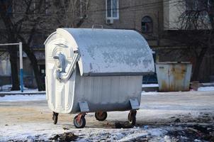 A silver garbage container stands near residential buildings in winter photo