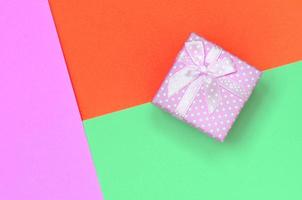 pequeña caja de regalo rosa sobre fondo de textura de papel de color turquesa pastel, rojo y rosa de moda foto