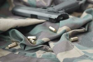 9mm bullets and pistol lie on folded camouflage green fabric. A set shooting range items or a self-defense kit photo