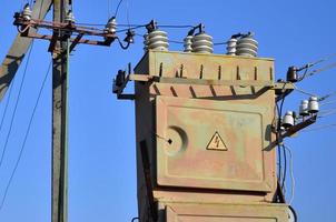 Old and obsolete electrical transformer against the background of a cloudless blue sky. Device for distribution of supply of high-voltage energy photo