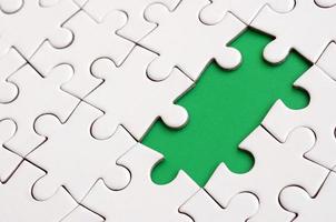 Close-up texture of a white jigsaw puzzle in assembled state with missing elements forming a green pad for text. Copy space photo