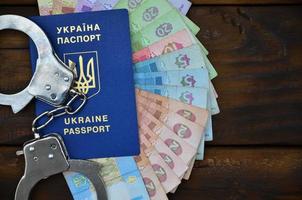 A photograph of a Ukrainian foreign passport, a certain amount of Ukrainian money and police handcuffs. Concept of illegal earnings of Ukrainian citizens abroad photo