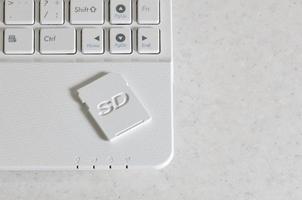 A compact SD memory card lies on a white netbook. The digital information storage device is ready for use. Concept of modern technologies photo