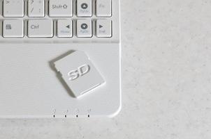 A compact SD memory card lies on a white netbook. The digital information storage device is ready for use. Concept of modern technologies photo