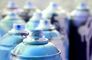 A lot of dirty and used aerosol cans of bright blue paint. Macro photograph with shallow depth of field. Selective focus on the spray nozzle photo