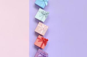 Small gift boxes of different colors with ribbons lies on a violet and pink color background photo