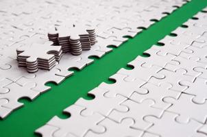 The green path is laid on the platform of a white folded jigsaw puzzle. The missing elements of the puzzle are stacked nearby. Texture image with space for text photo
