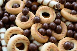 A lot of crispy sweet tubules, chocolate melting balls and yellow bagels lie on a wooden surface. Close up view photo