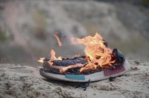 Burning sports sneakers or gym shoes on fire stand on sandy beach coast. Athlete burned out. Physical exertion during training concept photo