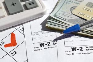 W-2 Wage and Tax statement blank with credit card on dollar bills, calculator and pen on calendar page with marked 15th April photo