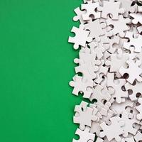 A pile of uncombed elements of a white jigsaw puzzle lies on the background of a green surface. Texture photo with copy space for text