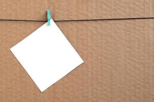 White blank card on rope on a brown cardboard background. Creative reminder, small sheet of paper on wooden clothespin, memo backdrop photo