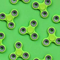 Many green fidget spinners lies on texture background of fashion pastel green color paper in minimal concept photo
