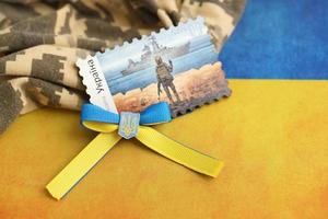 TERNOPIL, UKRAINE - SEPTEMBER 2, 2022 Famous Ukrainian postmark with russian warship and ukrainian soldier as wooden souvenir on army camouflage uniform and national flag photo