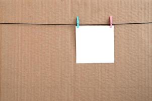 White blank card on rope on a brown cardboard background. Creative reminder, small sheet of paper on wooden clothespin, memo backdrop photo