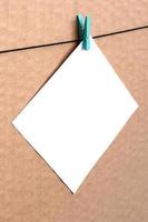 White blank card on rope on a brown cardboard background. Creative reminder, small sheet of paper on wooden clothespin, memo backdrop photo