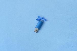 Brilliant blue usb flash memory card with a blue bow lies on a blanket of soft and furry light blue fleece fabric. Classic female gift design for a memory card photo