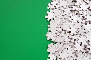 A pile of uncombed elements of a white jigsaw puzzle lies on the background of a green surface. Texture photo with copy space for text