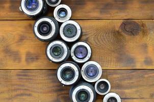 Several photographic lenses lie on a brown wooden background. Space for text photo