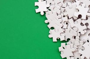 A pile of uncombed elements of a white jigsaw puzzle lies on the background of a green surface. Texture photo with copy space for text