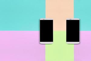 Two modern smartphones with black screens on background of fashion pastel pink, blue, coral and lime colors photo