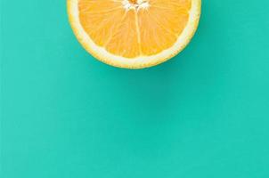 Top view of a one orange fruit slice on bright background in turquoise green color. A saturated citrus texture image photo