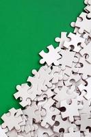 A pile of uncombed elements of a white jigsaw puzzle lies on the background of a green surface. Texture photo with copy space for text