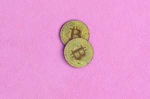 Two golden bitcoins lies on a blanket made of soft and fluffy light pink fleece fabric. Physical visualization of virtual crypto currency photo