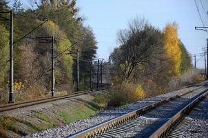 Autumn industrial landscape. Railway receding into the distance among green and yellow autumn trees photo