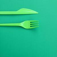 Disposable plastic cutlery green. Plastic fork and knife lie on a green background surface photo