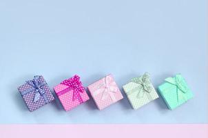 Small gift boxes of different colors with ribbons lies on a violet and pink background photo