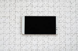 A modern big smartphone with a touch screen lies on a white jigsaw puzzle in an assembled state photo