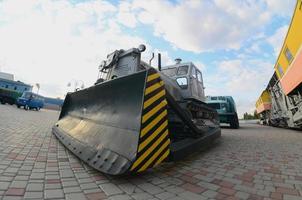 Photo of a gray bulldozer among the railway trains. Strong distortion from the fisheye lens