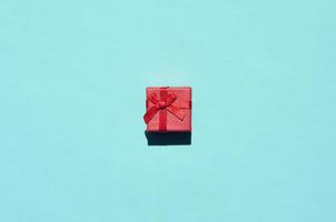 Small red pink gift box lie on texture background of fashion trendy pastel blue color paper in minimal concept photo