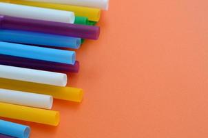 Many colorful straws for drinks lies on a bright orange background surface photo