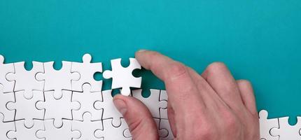 The hand folds a white jigsaw puzzle against the background of the blue surface. Texture photo with space for text