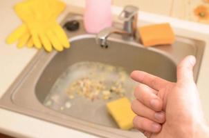 la mano apunta al fregadero de la cocina sucio con muchas partículas de comida antes de la limpieza foto