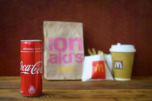 KHARKOV, UKRAINE - DECEMBER 9, 2020 McDonald's take away paper bag and french fries with coca cola can on wooden table photo