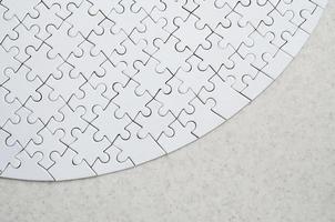 A white jigsaw puzzle in the complete form lies on a treated stone surface. Textured image with copy space photo
