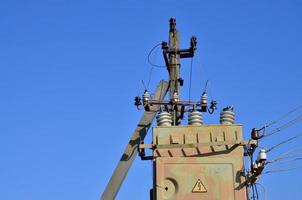 Old and obsolete electrical transformer against the background of a cloudless blue sky. Device for distribution of supply of high-voltage energy photo