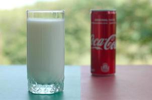 KHARKOV. UKRAINE - MAY 2, 2019 Coca cola red tin can and cup of fresh milk on colored surface photo