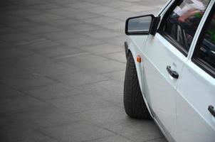 Diagonal view of a white glossy car that stands on a square of gray tiles photo