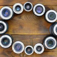 Several photographic lenses lie on a brown wooden background. Space for text photo