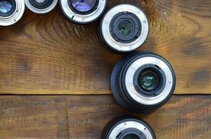 Several photographic lenses lie on a brown wooden background. Space for text photo