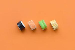 diferentes tipos de rollos de sushi asiáticos sobre fondo naranja. minimalismo vista superior plana con comida japonesa foto