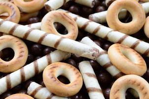 A lot of crispy sweet tubules, chocolate melting balls and yellow bagels lie on a wooden surface. Close up view photo