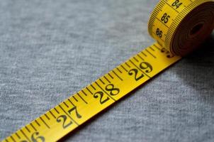 Yellow measuring tape lies on a gray knitted fabric photo