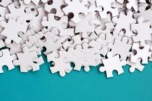 A pile of uncombed elements of a white jigsaw puzzle lies on the background of a blue surface. Texture photo with copy space for text