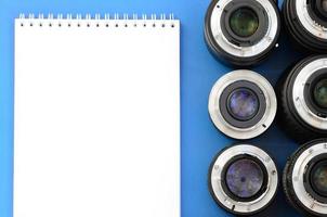 Several photographic lenses and white notebook lie on a bright blue background. Space for text photo